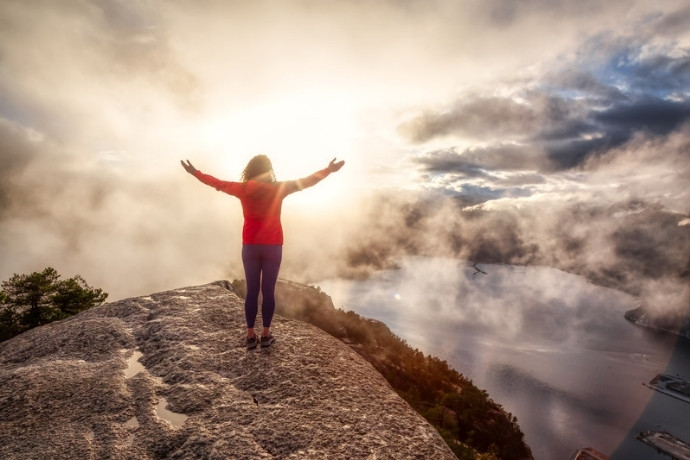 A hiker with arms raised on a mountain summit above the clouds