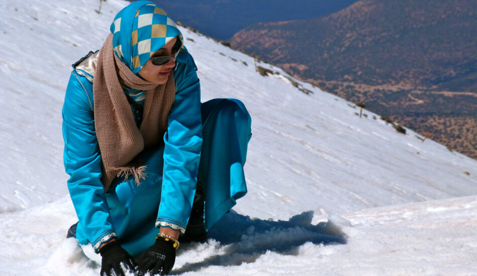 Woman in a bright blue kaftan playing in the snow on a mountain slope in Morocco