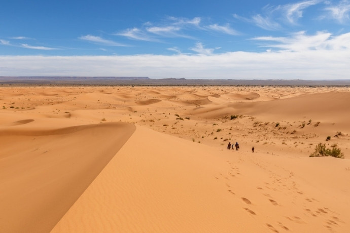 Sweeping Sahara dune ridges and walkers under a blue sky in Morocco